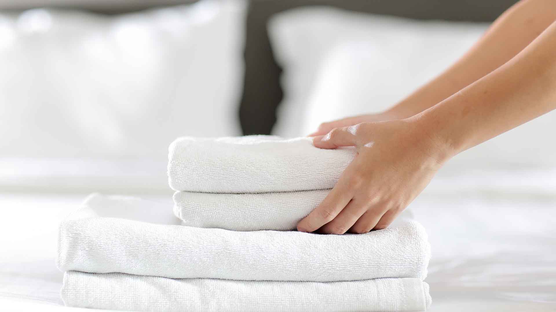 A person stacking towels on top of a bed.