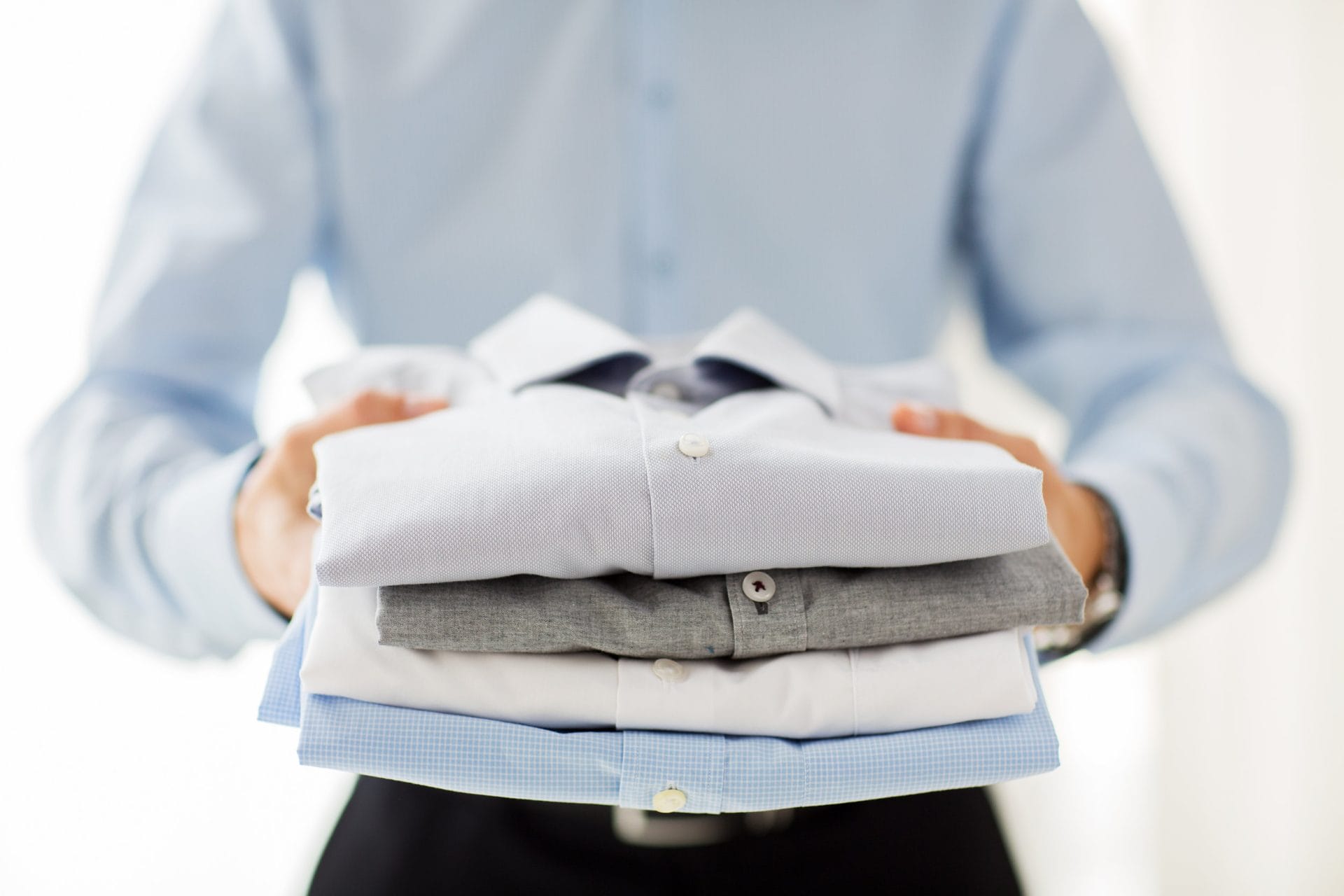 A man is holding a stack of shirts.