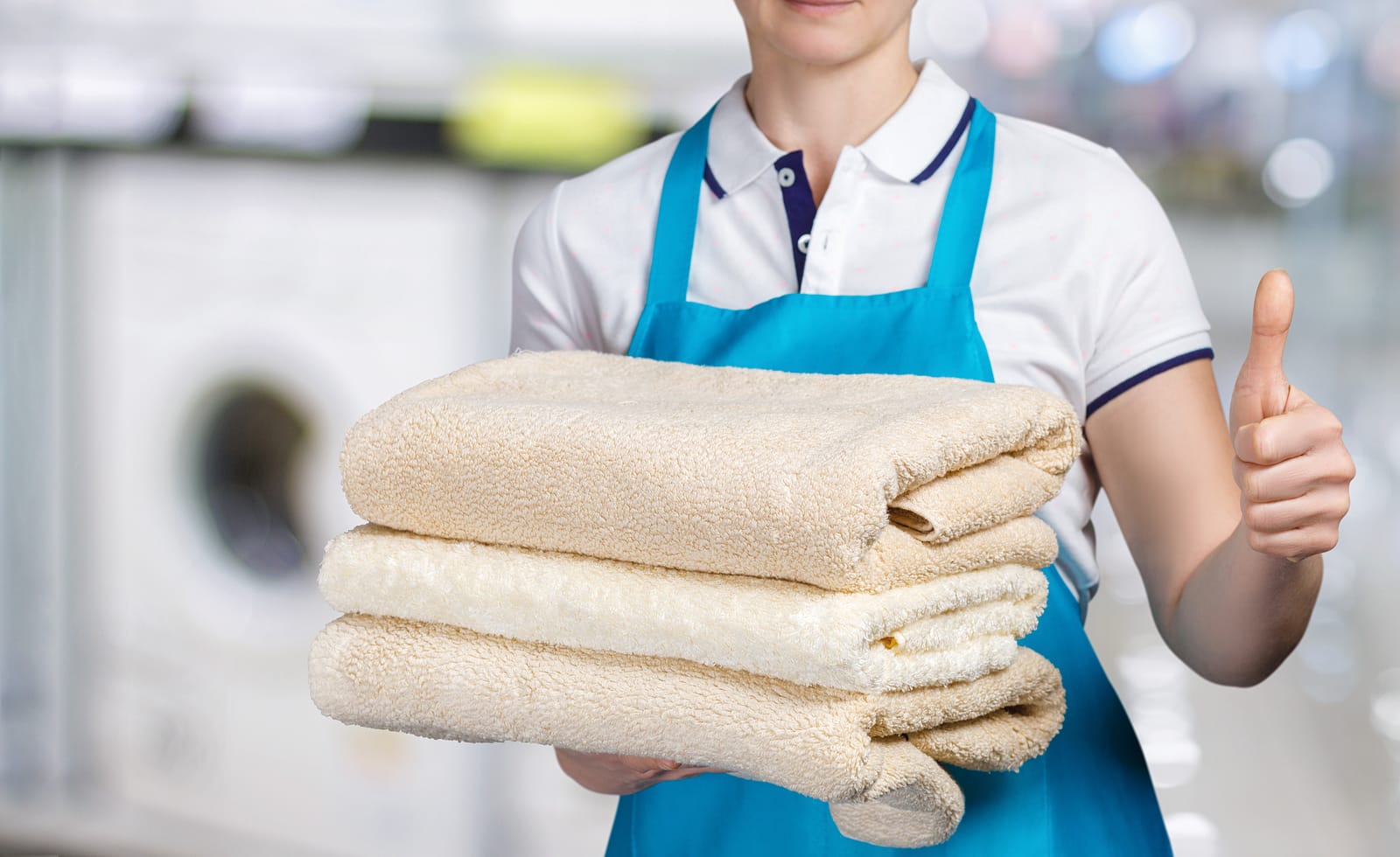 A woman holding a stack of towels in front of a washing machine.